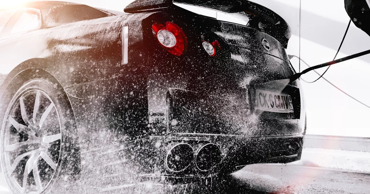 Professional in blauw uniform die een witte auto wast met een hogedrukreiniger