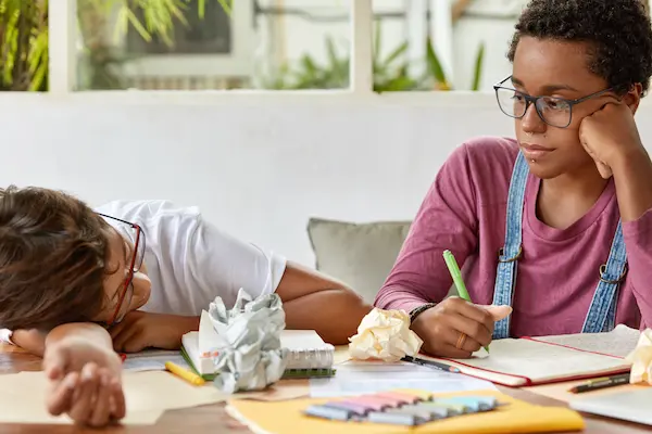 askaide-dark-skinned-female-student-wears-transparent-glasses-looks-seriously-tired-classmate-work-together-course-paper-pose-desk-with-papers-notepad-collaborate-learn-material