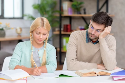 Een jong meisje maakt haar huiswerk thuis met hulp van een tutor die haar aandachtig begeleidt.